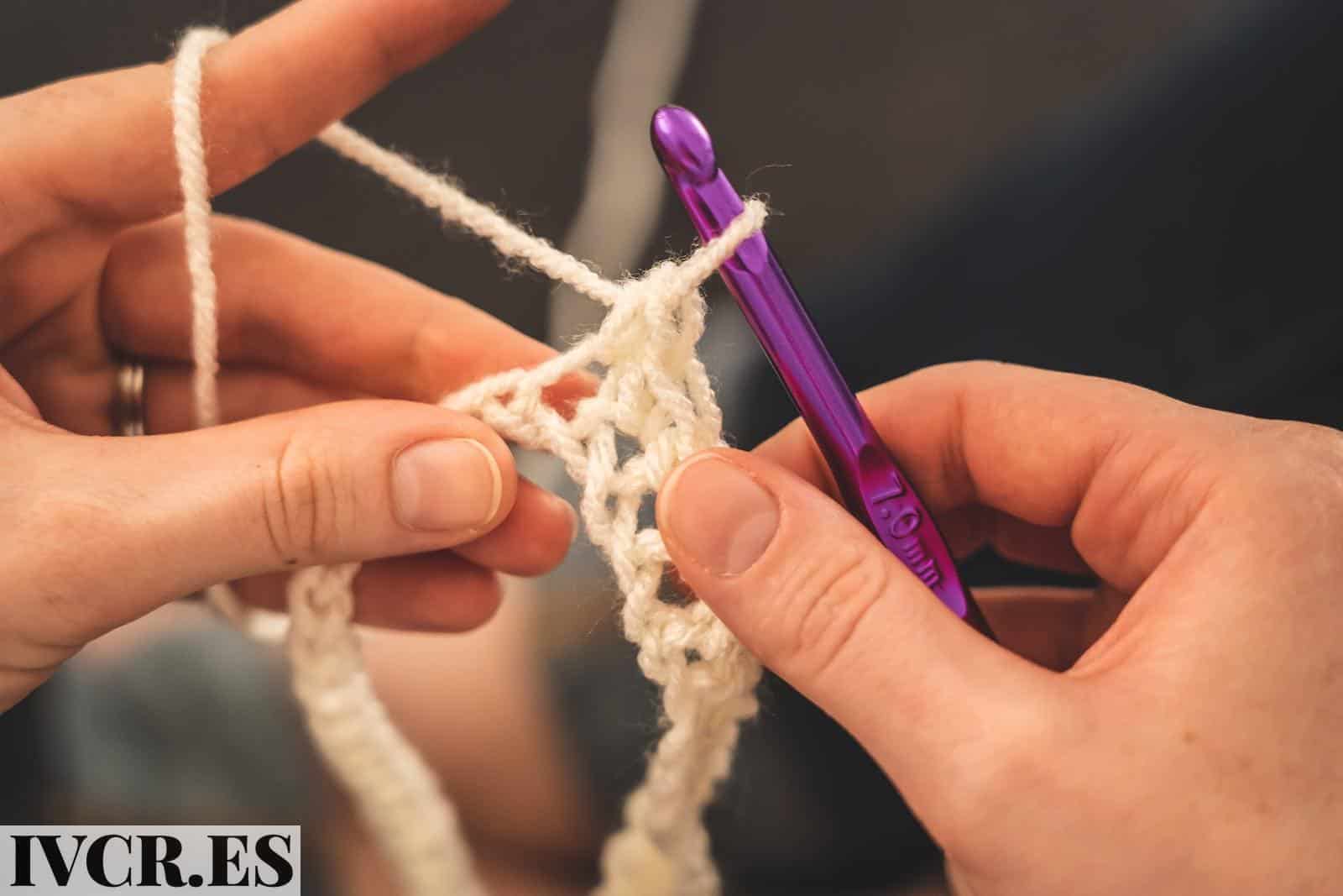 Person Holding Purple Crochet Hook and White Yarn